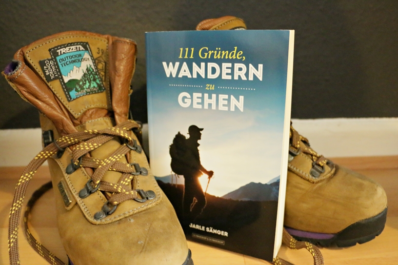 Titelbild von dem Buch 111 Gründe, wandern zu gehen mit Wanderschuhen im Hintergrund